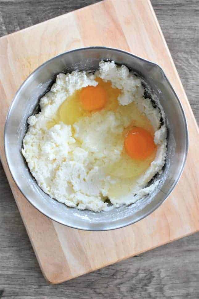 Two eggs added to the cheese mixture in a mixing bowl