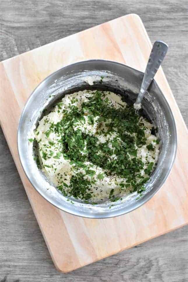 Chopped parsley added to the cheese mixture in a mixing bowl