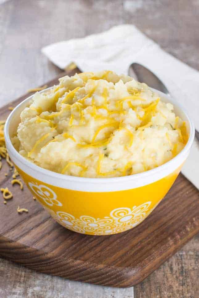 Mashed potatoes in a yellow bowl with extra cheese on top