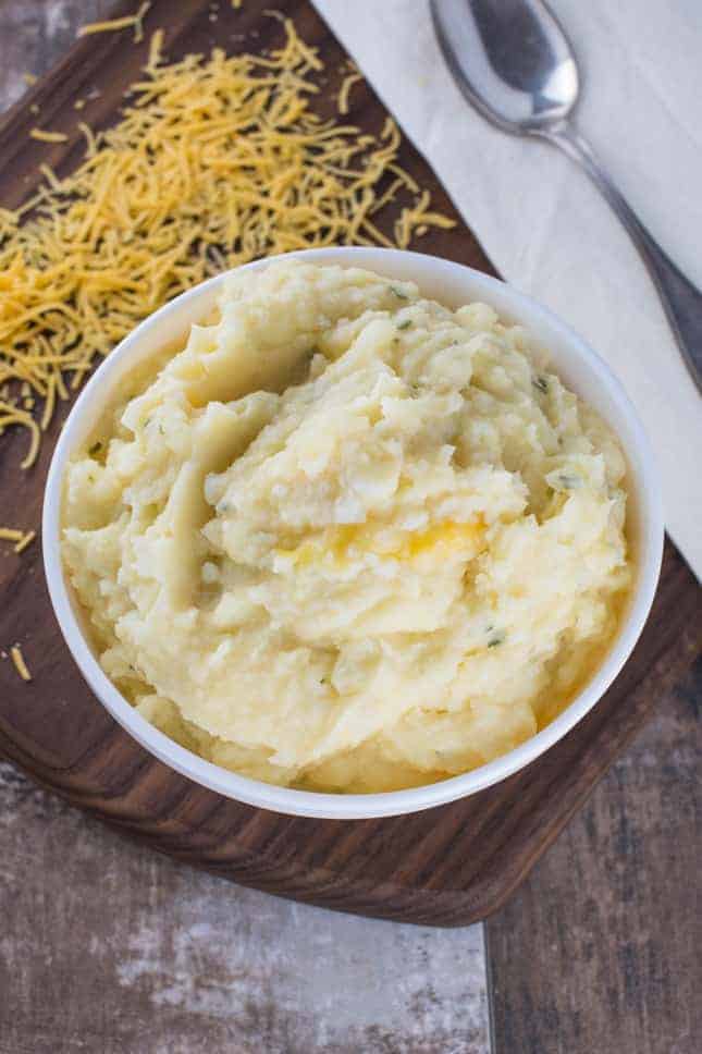 overhead of mashed potatoes in a bowl with shredded cheddar behind it