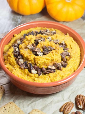 hummus in an orange bowl with grahams, pecans, cinnamon sticks and pumpkins around it