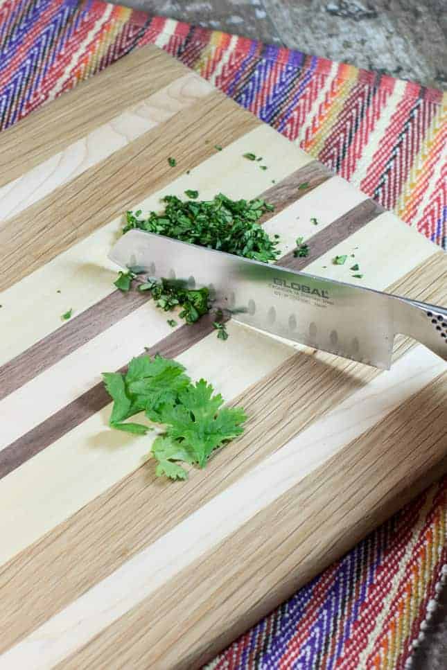 Chopping cilantro on a wooden cutting board with a knife.