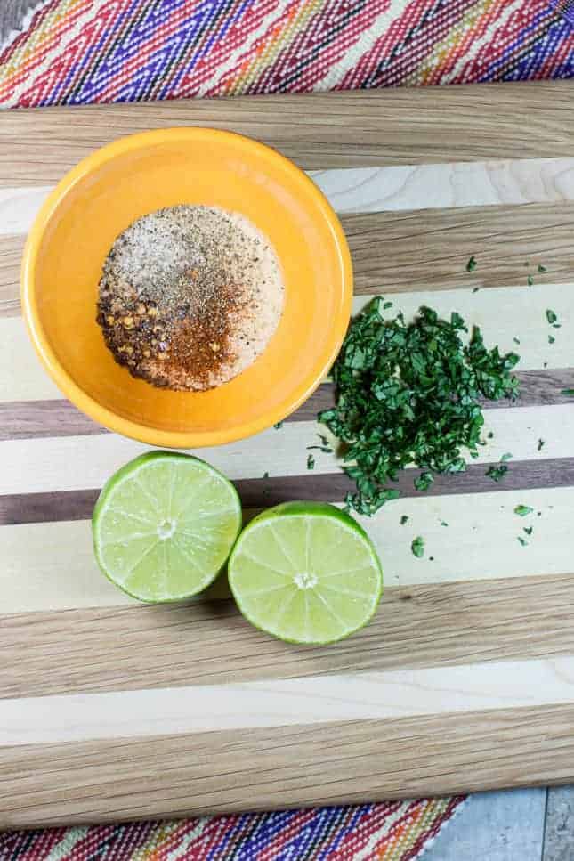 Dry seasonings, cilantro and lime on a cutting board.