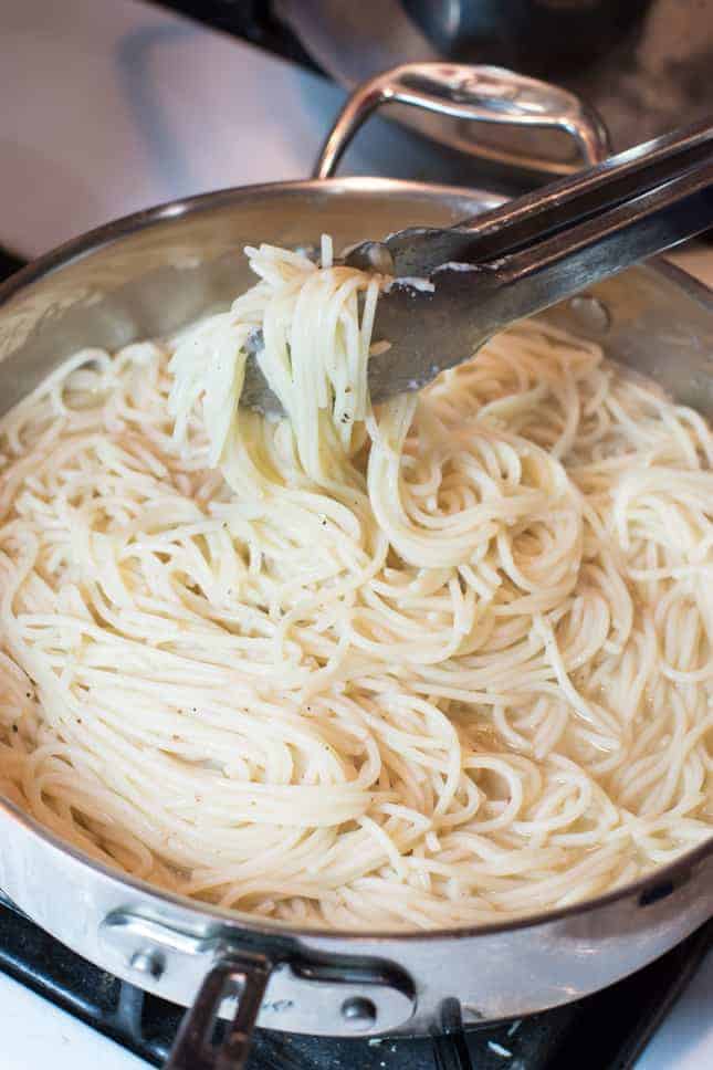 tossing pasta with tongs in the sauté pan
