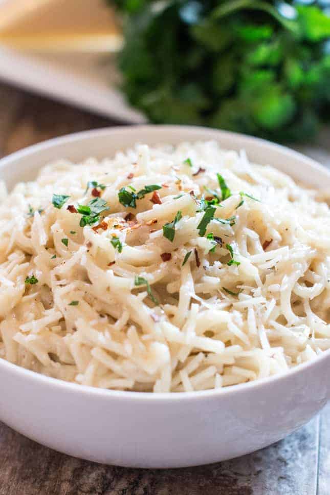 gluten-free cacio e pepe in a white bowl garnished with fresh parsley and crushed red pepper flakes
