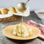 using a ladle to pour gravy onto mashed potatoes on a plate