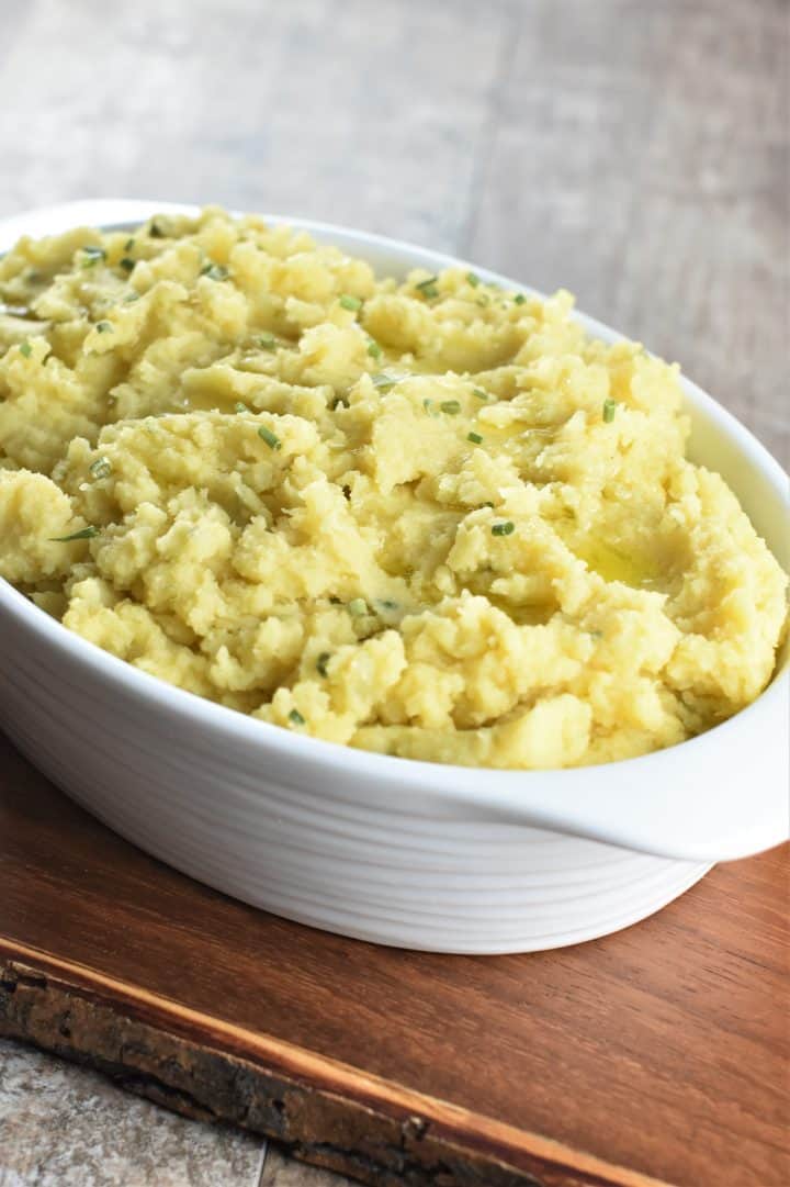 Cheesy vegan mashed potatoes garnished with chives in white serving bowl