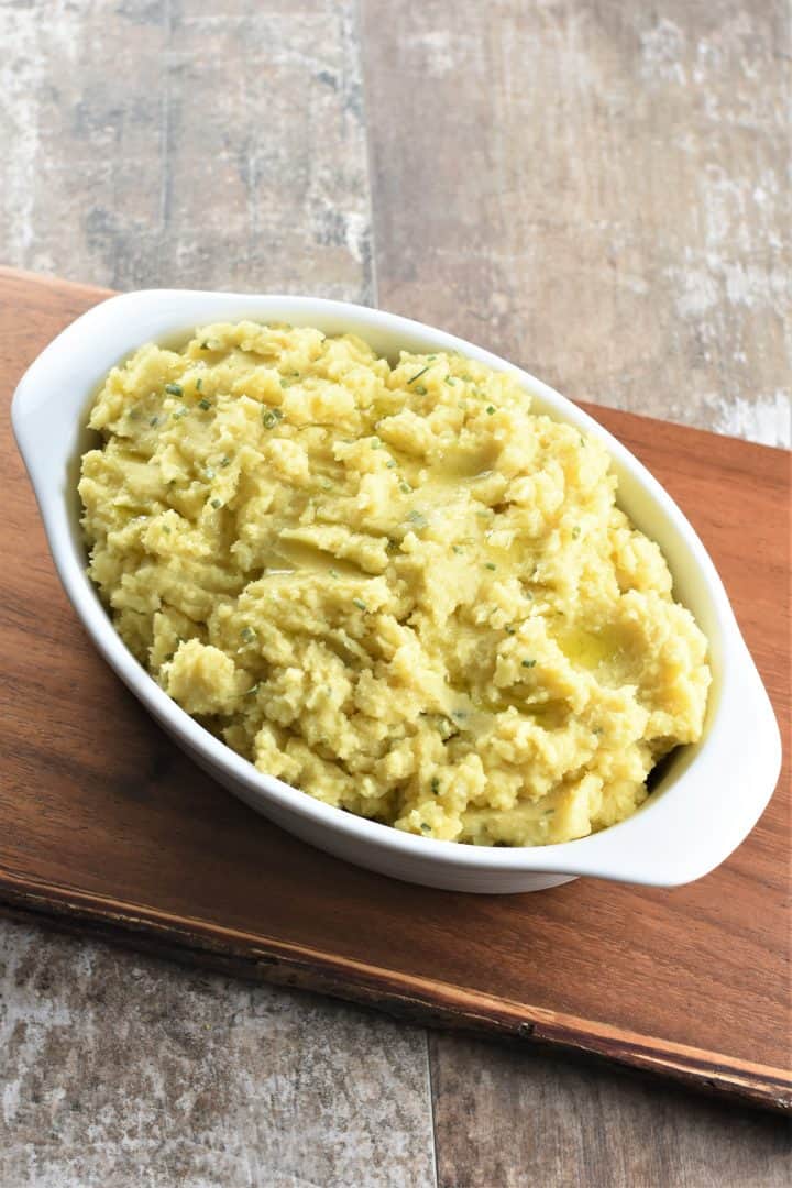 overhead of mashed potatoes in white serving bowl on wooden board