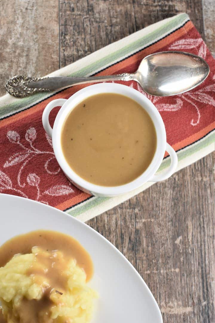 Chickpea Flour Gravy in a white serving bowl with a spoon and a partial view of mashed potatoes with the gravy