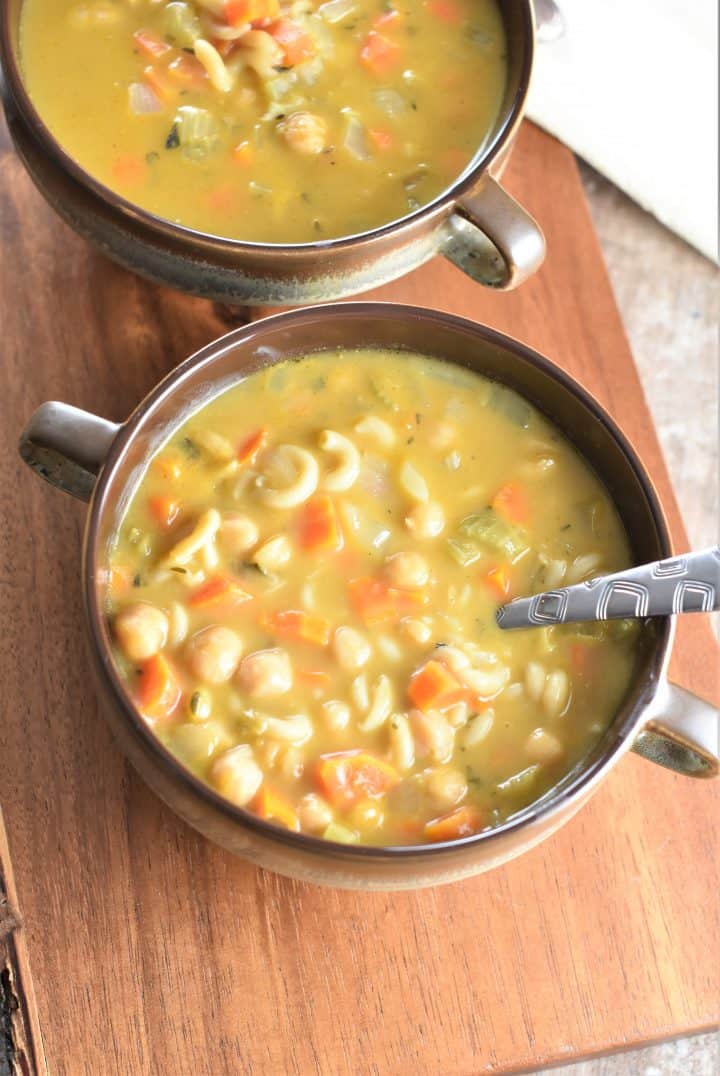 two bowls of soup on a wooden board with a spoon in the front one