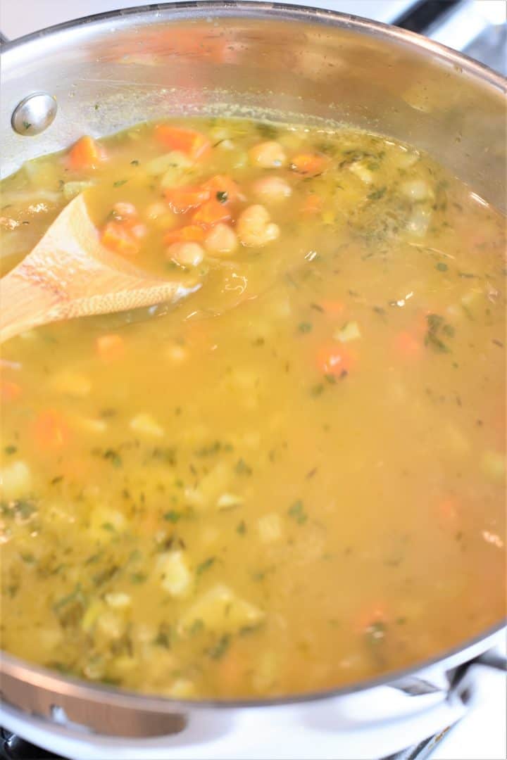 Scooping chickpeas, veggies and broth with a wooden spoon