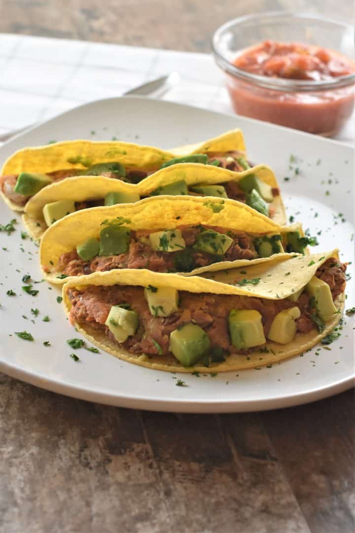 front closeup view of tacos on a white plate garnished with cilantro and salsa in the background