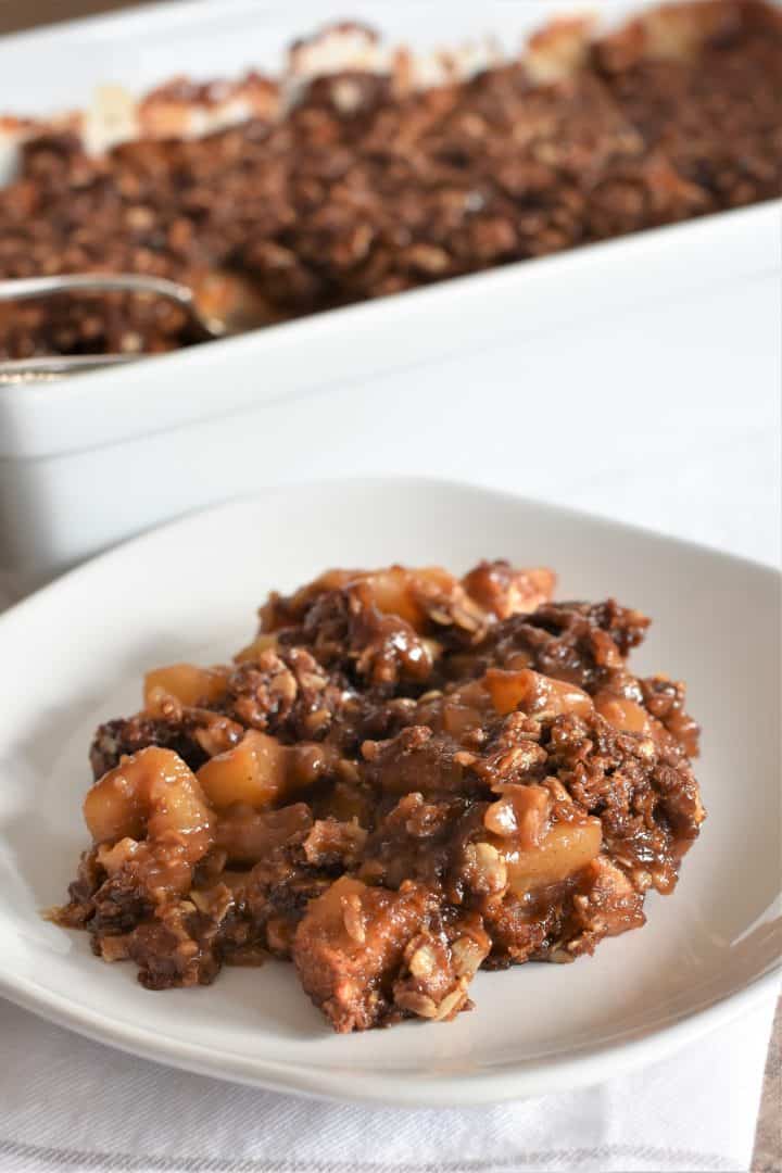 apple crisp on a plate with the baking dish with the rest in the background