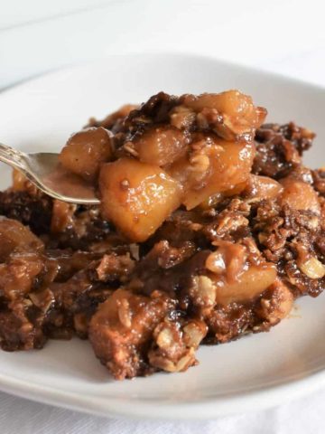 Vegan apple crisp being scooped up on a fork from a plate