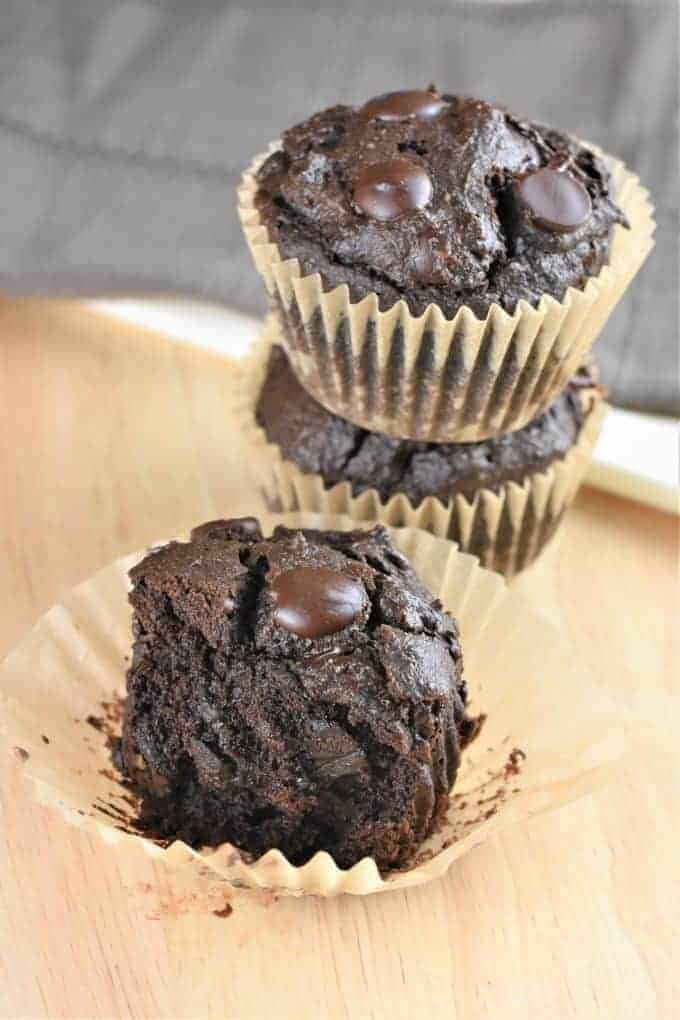 half of a muffin on a parchment baking cup with two stacked up behind it