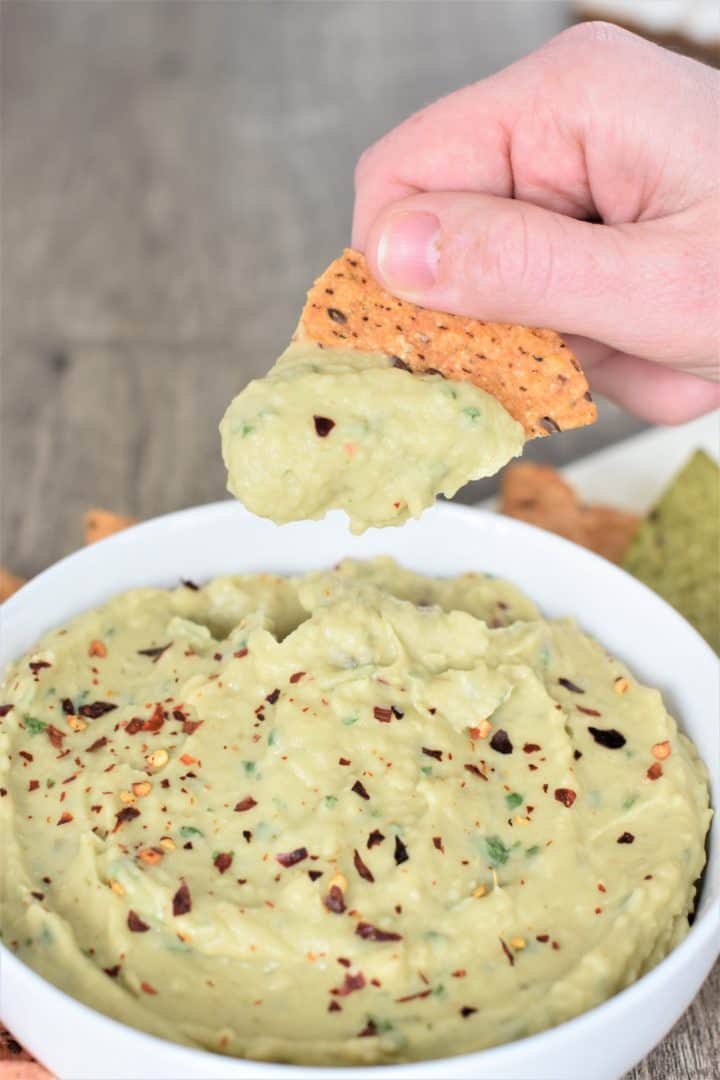 Scooping hummus with a chip from a white bowl