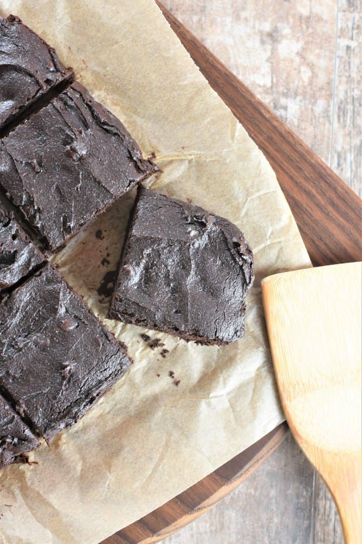 overhead of cut brownie piece on parchment on a wooden board with parts of other brownies in view