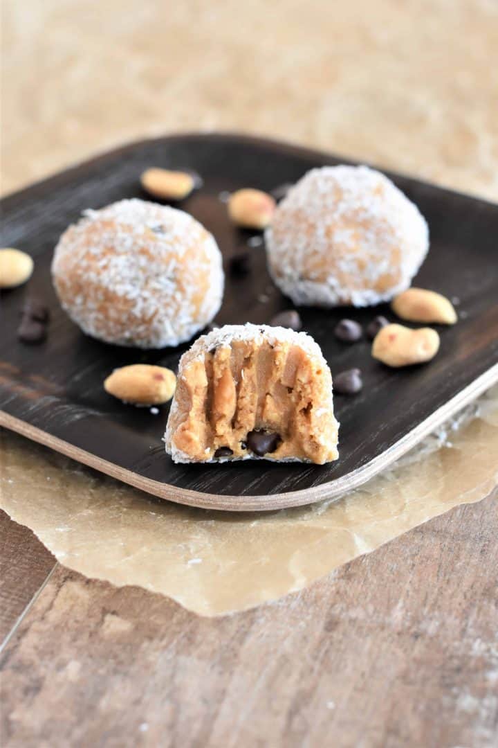 3 peanut butter balls rolled in coconut on a plate with some peanuts and chocolate chips around