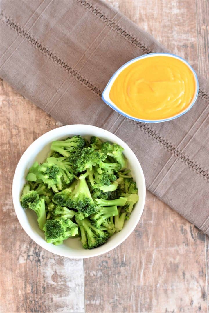 small bowl of broccoli with cup of cheese sauce next to it