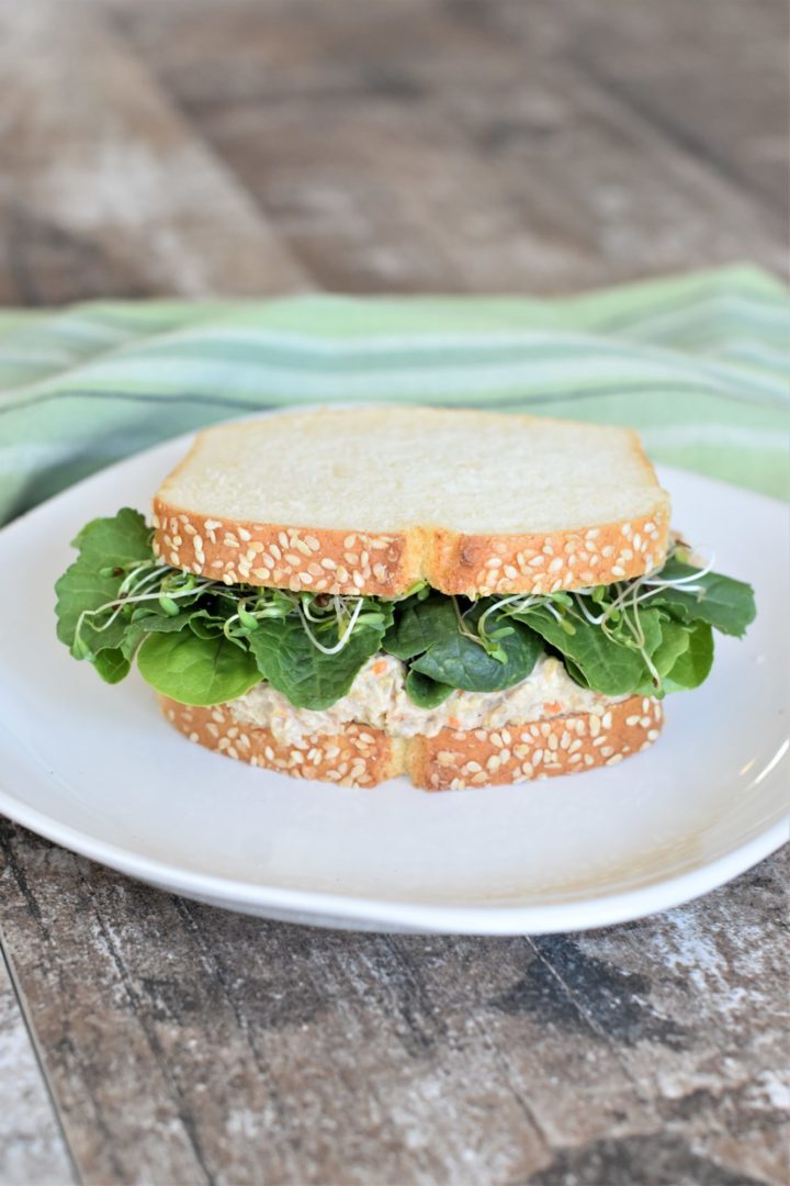 front view of chickpea salad sandwich with lettuce and microgreens on a white plate 