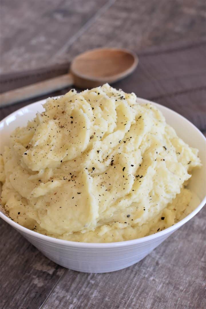 front view of vegan cream cheese mashed potatoes in a white bowl with wooden spoon behind them