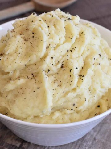 mashed potatoes in a white serving bowl with a wooden spoon behind it