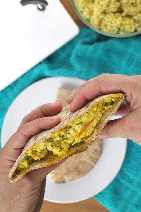 Hands holding half of a pita with tofu egg salad