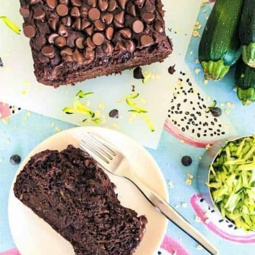 piece of chocolate zucchini bread on a plate with a fork and the rest of the loaf behind it