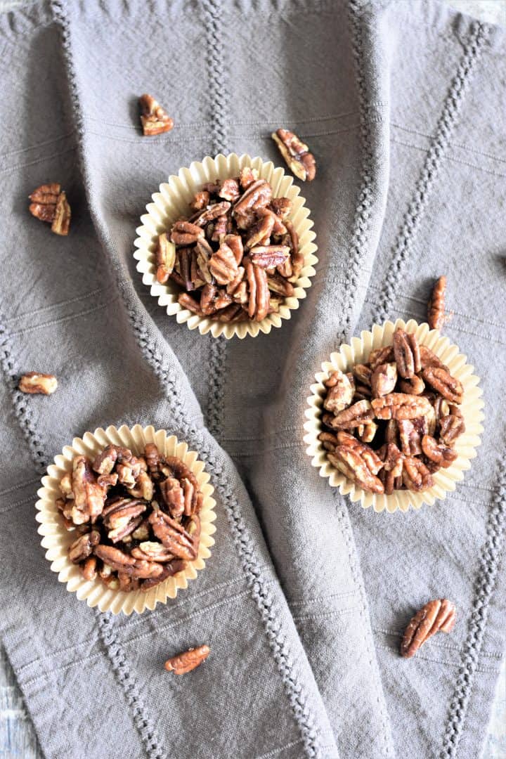 pecans in three parchment baking cups on a kitchen towel with more pecans sprinkled on the towel