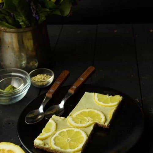 two lemon bars on a black plate with two spoons