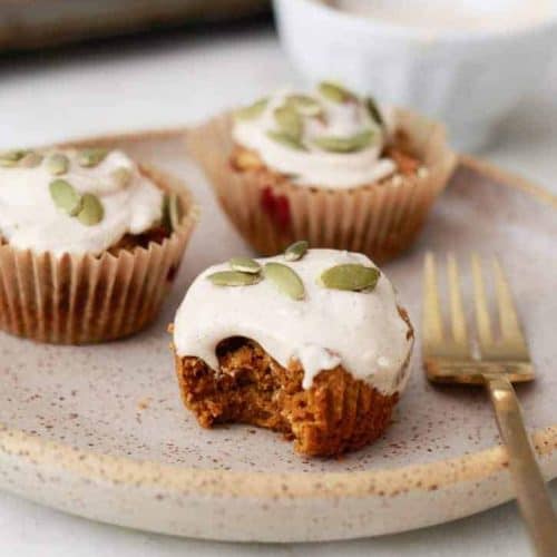 three pumpkin muffins on a plate with a fork and a piece taken off the one in front