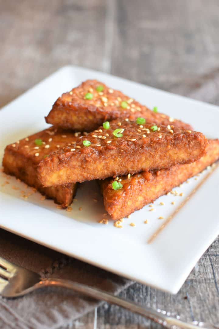 Baked tempeh on a dish garnished with toasted sesame seeds and scallions