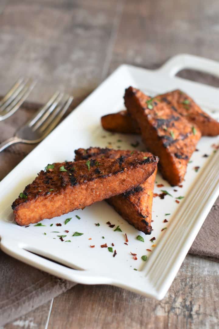 grilled tempeh on a white platter garnished with fresh parsley and red pepper flakes