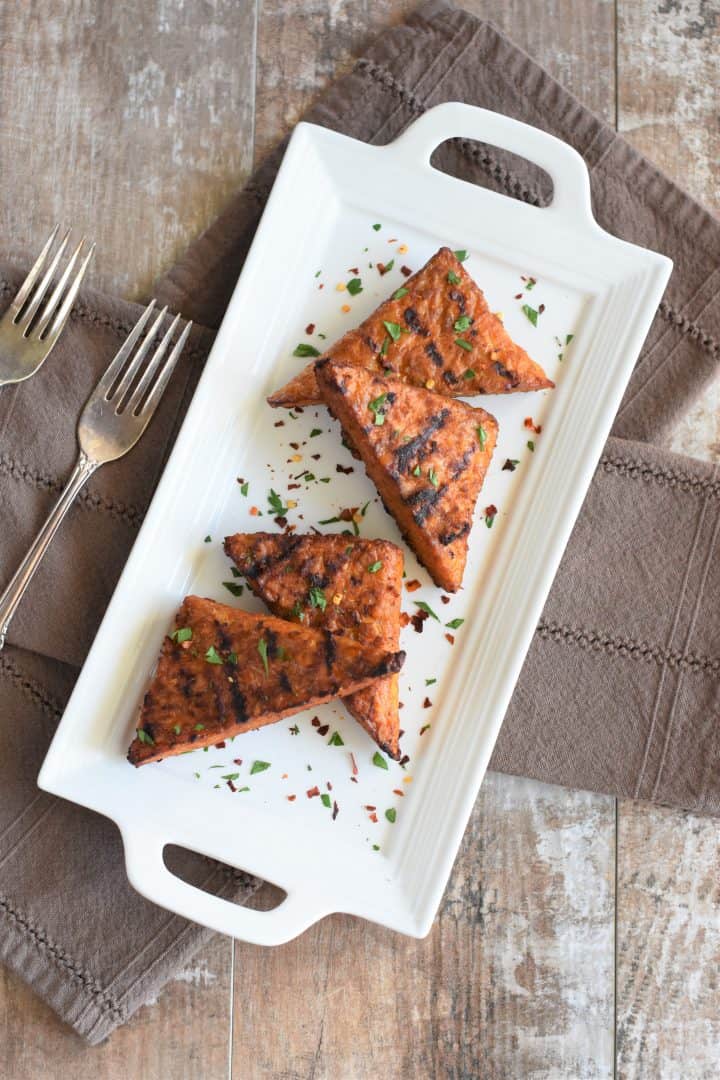 overhead view of grilled tempeh on white platter garnished with parsley and red pepper flakes