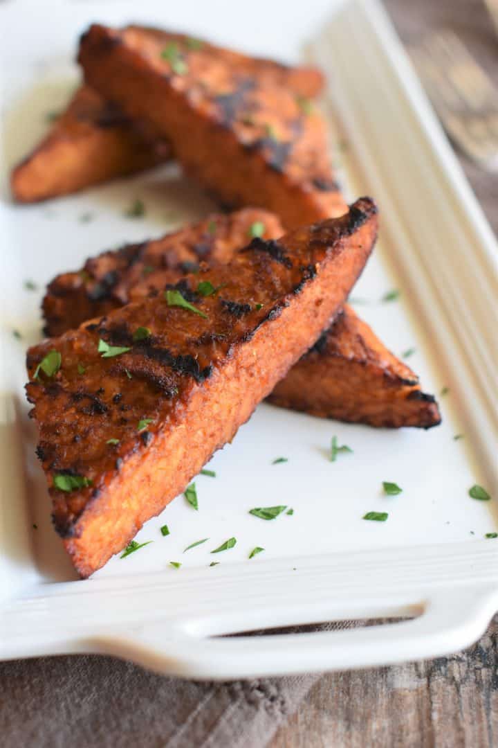 Close up view of grilled tempeh on a white platter garnished with parsley