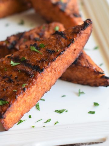 two pieces of grilled tempeh steaks on a white platter with some blurred out behind them