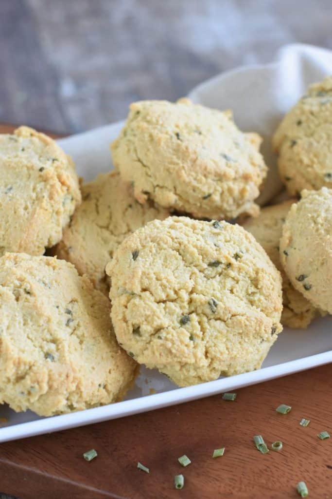 close up of vegan almond flour biscuits on a white serving dish on a wooden board with chives in front