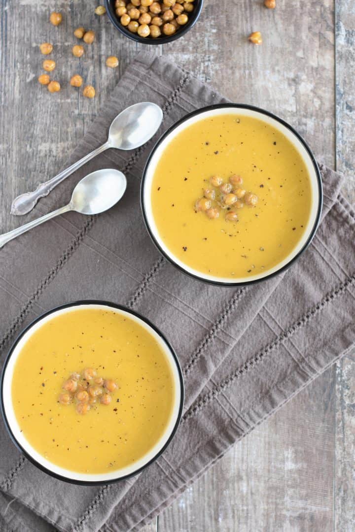 overhead view of two bowls of soup topped with roasted chickpeas and black pepper with two spoons next to them