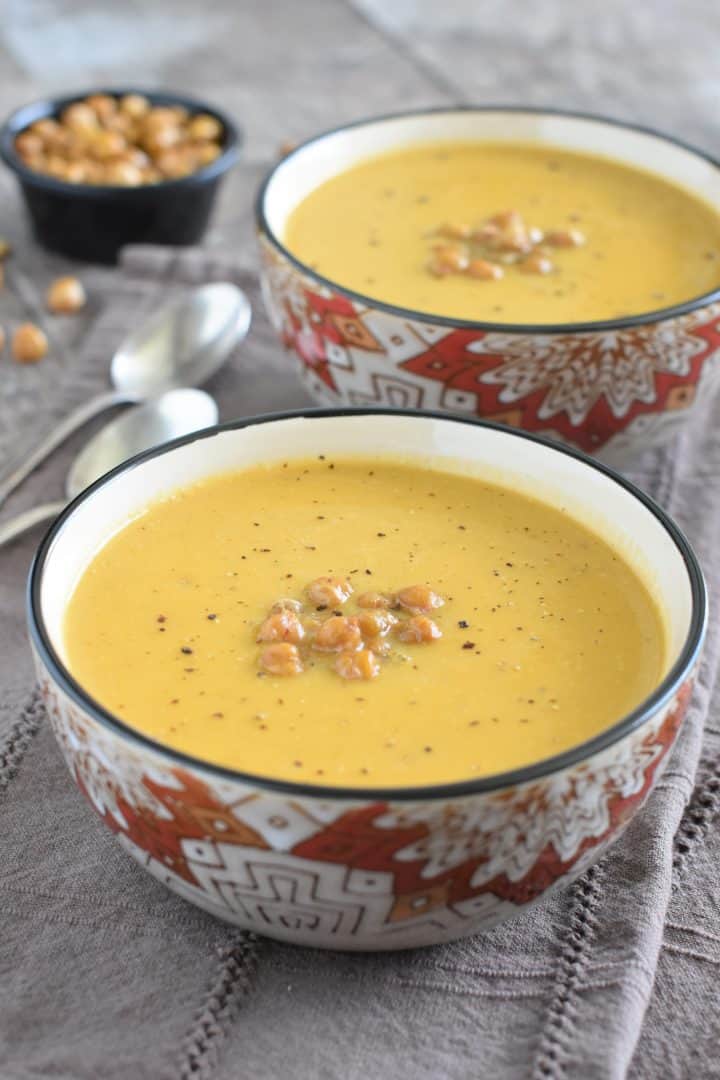 vegan butternut squash soup in two bowls with the front one in view, both are topped with roasted chickpeas and black pepper