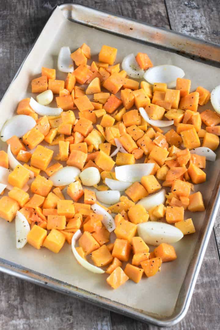 Seasoned butternut squash, onion and garlic on a baking sheet ready to be cooked