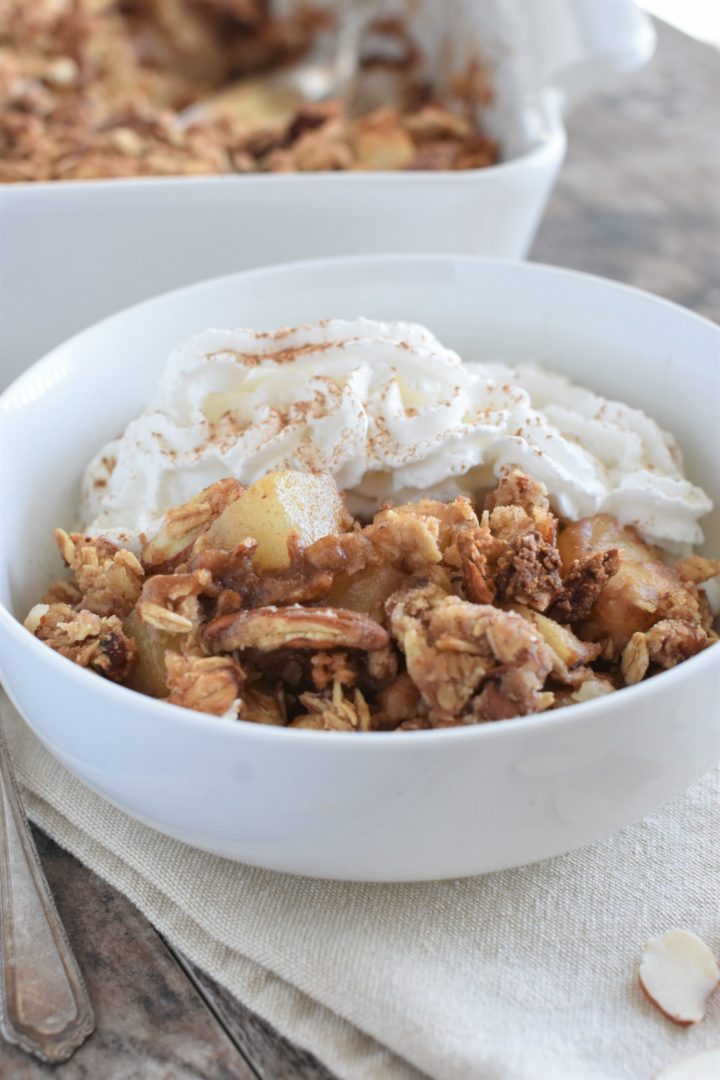 Front view of baked dessert in white bowl with some coconut whipped cream and the rest in the baking dish behind it