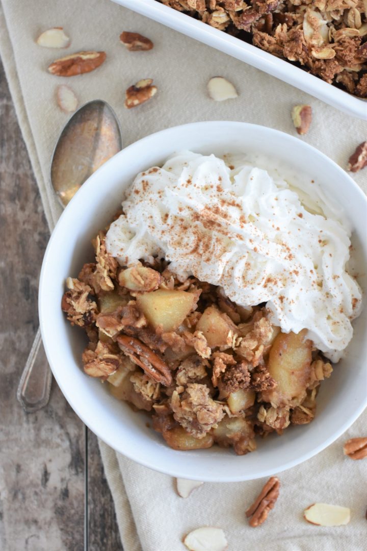 overhead of pear crisp in a white bowl with a spoon next to it and part of the baking dish with the rest behind it