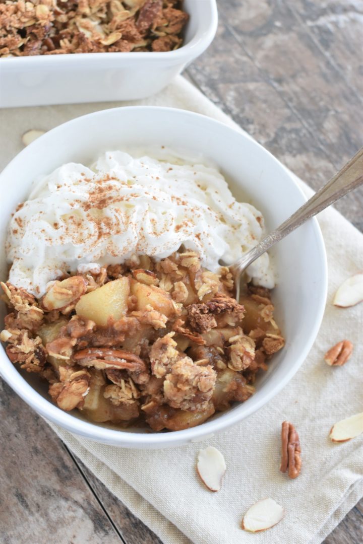 baked pear dessert in a white bowl with coconut whipped topping and a spoon in the bowl