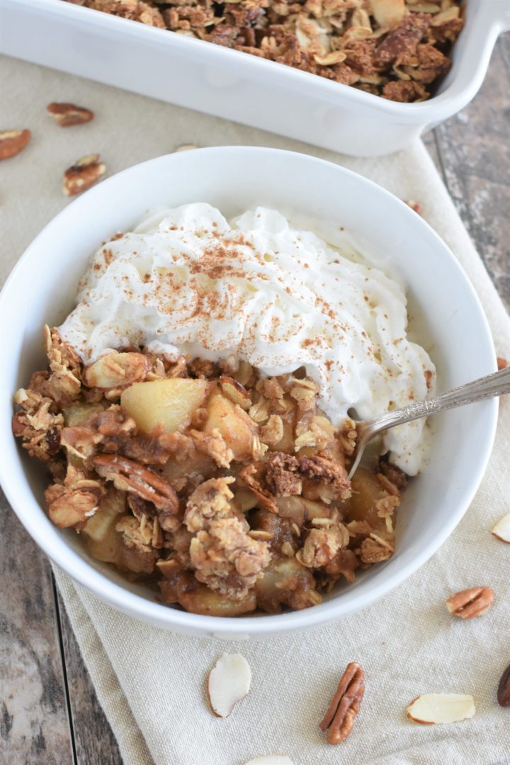 overhead of pear dessert in white bowl with coconut whipped topping and a spoon in the bowl