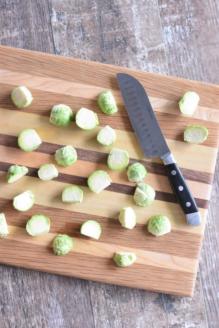 Brussels sprouts cut in half on a cutting board with knife next to them