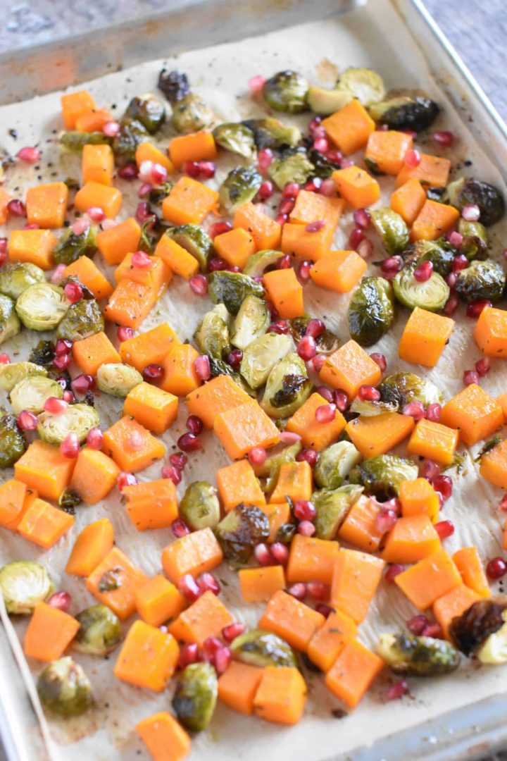 Pomegranate arils added to roasted butternut squash and Brussels sprouts on baking sheet