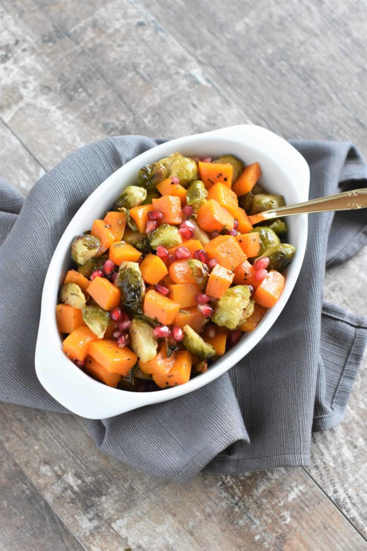 overhead of roasted butternut squash and Brussels sprouts with pomegranate in a white serving dish