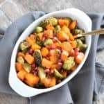 overhead of butternut squash and Brussels sprouts in white baking dish with a spoon in it