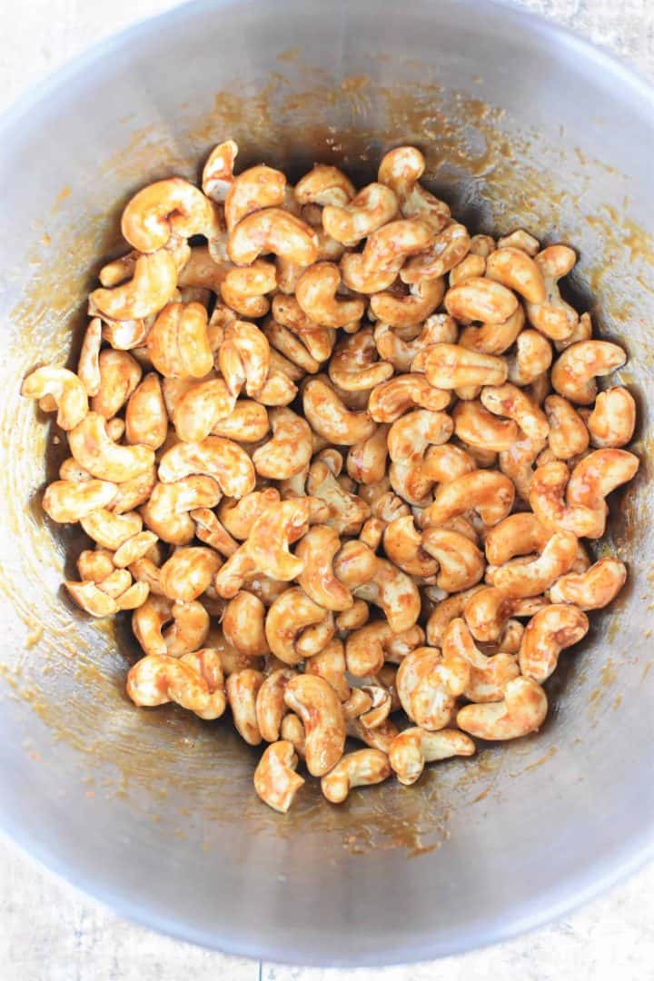 Date syrup, cayenne pepper and salt mixed into the cashews in a mixing bowl