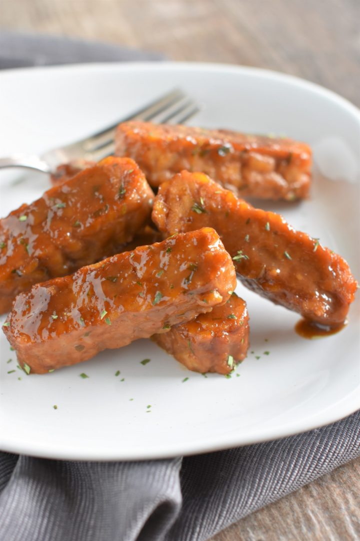 Close up of tempeh on white dish with fork on plate and extra tarragon garnish